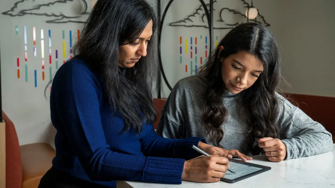 دو زن در حال کار با تبلت پشت میزی با پس‌زمینه‌ی یک دیوار هنری رنگارنگ