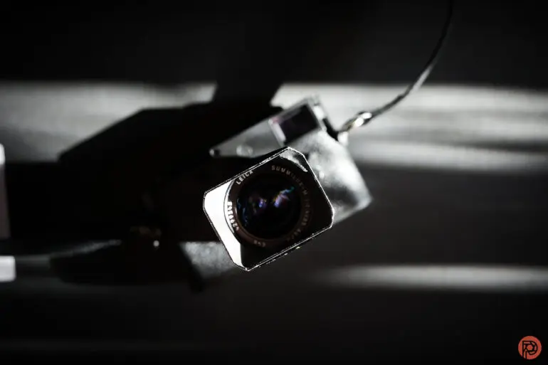 نمای نزدیک از لنز دوربین با نورپردازی درام و سایههای برجسته بر پسزمینه.