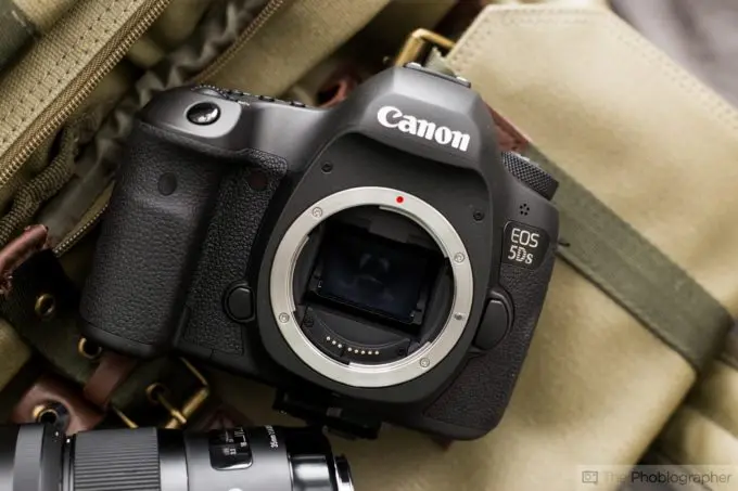 نمای نزدیک از بدنه دوربین کانون EOS 5DS روی سطح خاکی، با لنز دوربین در کنار آن.
