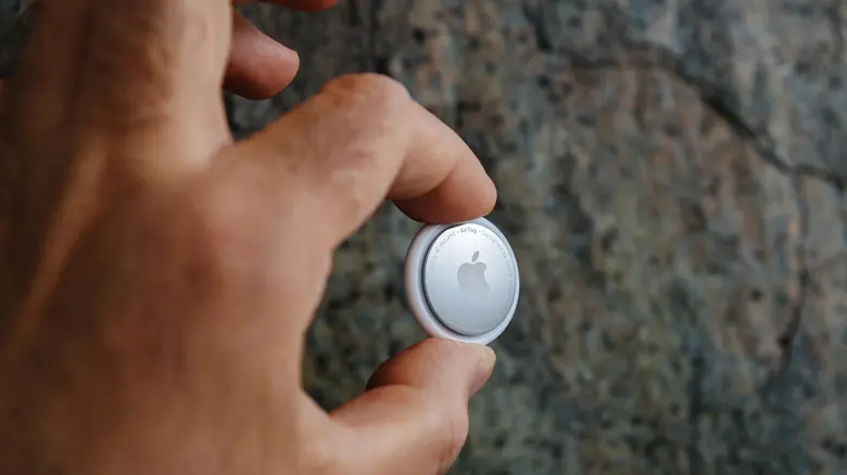 دست در حال نگه داشتن AirTag بر روی پس‌زمینهٔ تاریک