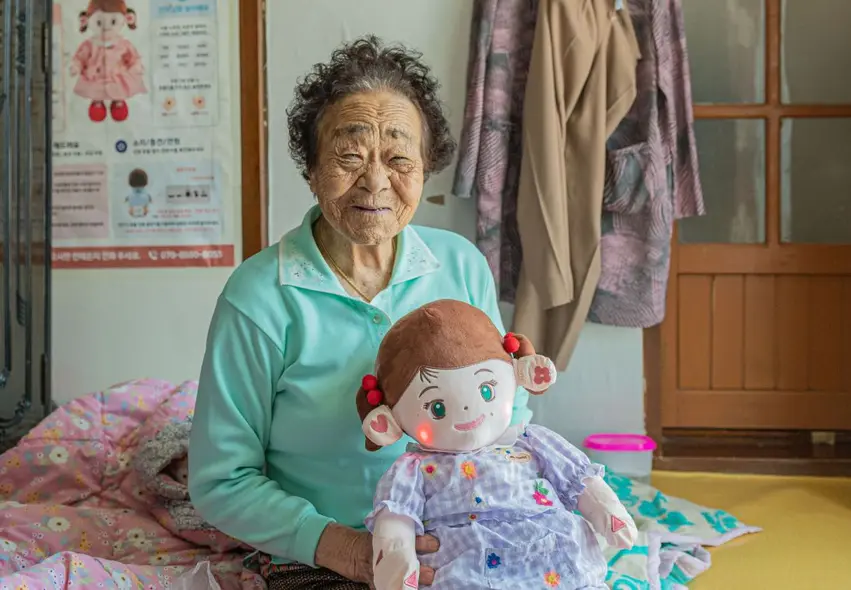 یک زن مسن ربات کمکی نرم‌پذیر Hyodol مجهز به هوش مصنوعی را در دست دارد. این دستگاه برای همراهی ۲۴ ساعت در روز با افراد تنها طراحی شده است تا حمایت عاطفی و نظارت بر مراقبت‌های بهداشتی ارائه دهد.