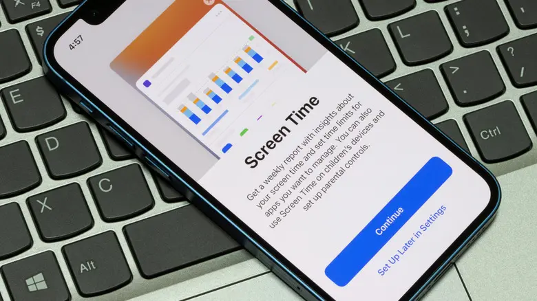 آیفونی که روی صفحه‌کلید لپ‌تاپ قرار دارد و صفحه تنظیمات زمان‌کاری (Screen Time) را نشان می‌دهد