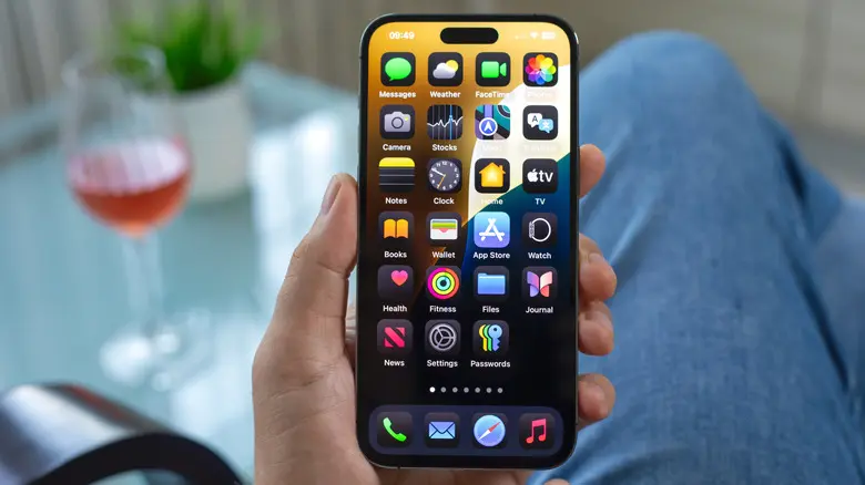 فردی که iPhone را در دست چپ خود نگه داشته و در حالی که بر سر میزی نشسته است
