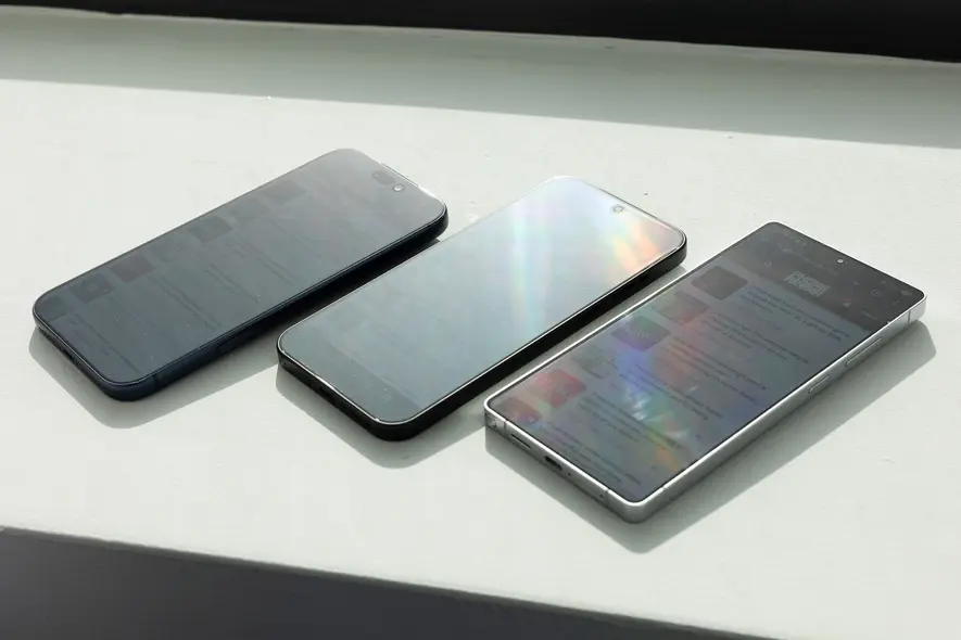 گوشی‌ها روی شیلنگ پنجره در نور مستقیم خورشید که درخشندگی شدید صفحه نمایش را نشان می‌دهند.