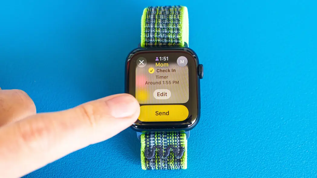 تصویر نمای نزدیک از اپل واچ SE روی پسزمینه آبی روشن که مراحل تنظیم و ارسال اعلان Check In در watchOS 11 را نشان میدهد