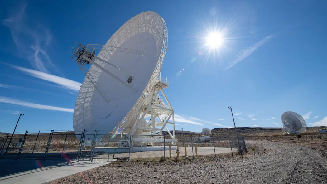 یک آنتن بزرگ سفید به سمت چپ صفحه جهت‌دار است و خورشید در آسمان آبی پشت آن قرار دارد