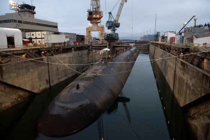 زیرآبی مشکی در آب تاریک و در میان دیوارهای بتنی لنگر انداخته شده است؛ جرثقیل‌ها در پس‌زمینه دیده می‌شوند.