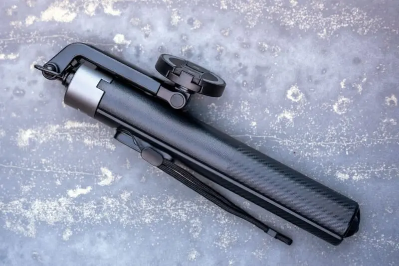 یک سه‌پایه سیاه، جمع‌وجور با نگهدارنده گوشی که جمع شده و بر روی سطح خاکستری با بافت و لکه‌های نازک قرار گرفته است.