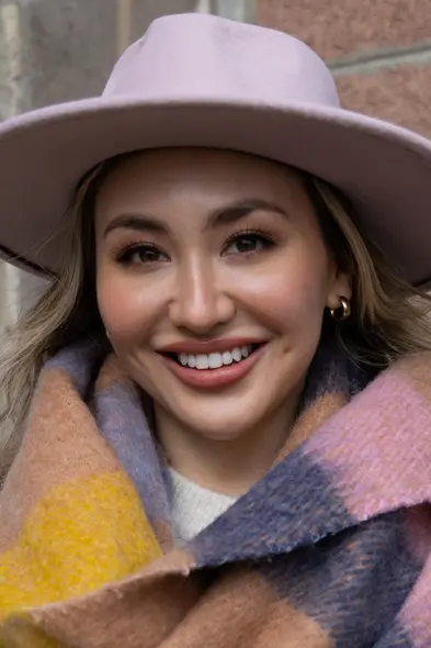 شخص خندان با کلاه لبه‌پهن و شال شطرنجی رنگارنگ در پس‌زمینهٔ آجری. شات با Canon R6 II. اعتبار تصویر: Brittany Smith