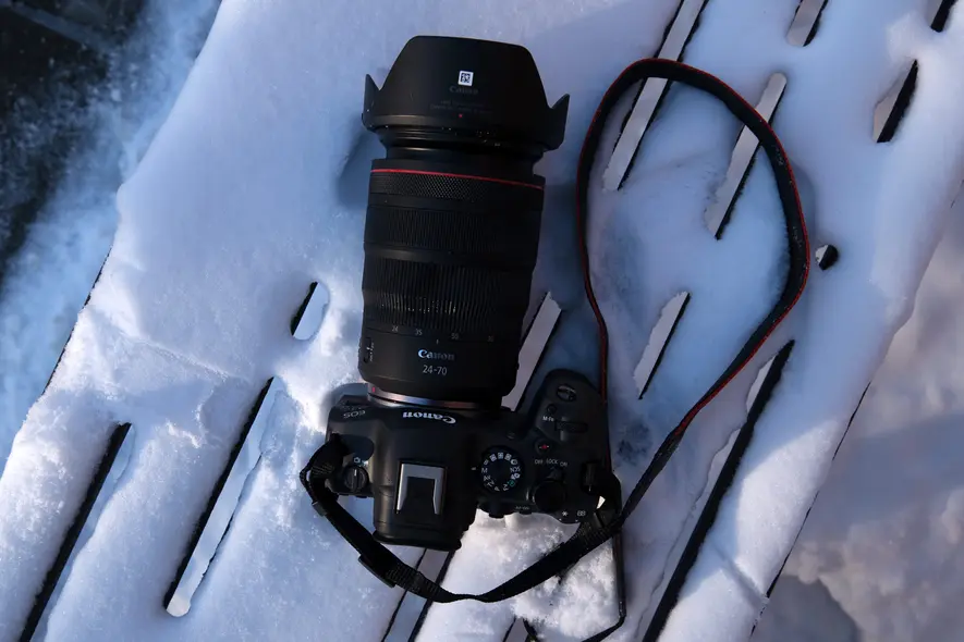 دوربین کانن با لنز زوم و بند که روی سطح چوبی پوشیده از برف قرار دارد.