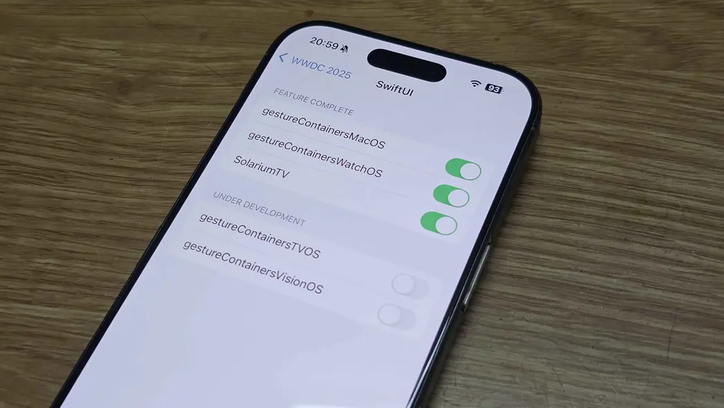صفحه نمایش گوشی فهرستی از وضعیت ویژگی‌ها با سوئیچ‌های روشن/خاموش نشان می‌دهد؛ برخی ویژگی‌ها تکمیل شده‌اند و برخی دیگر در حال توسعه، بر روی سطح چوبی