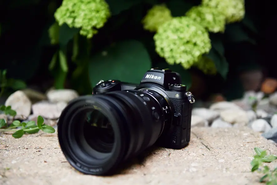 دوربین نیکون با لنز بزرگ بر روی سطح سنگی است و در پس‌زمینه گیاهان سبز برگ‌دار دیده می‌شود.