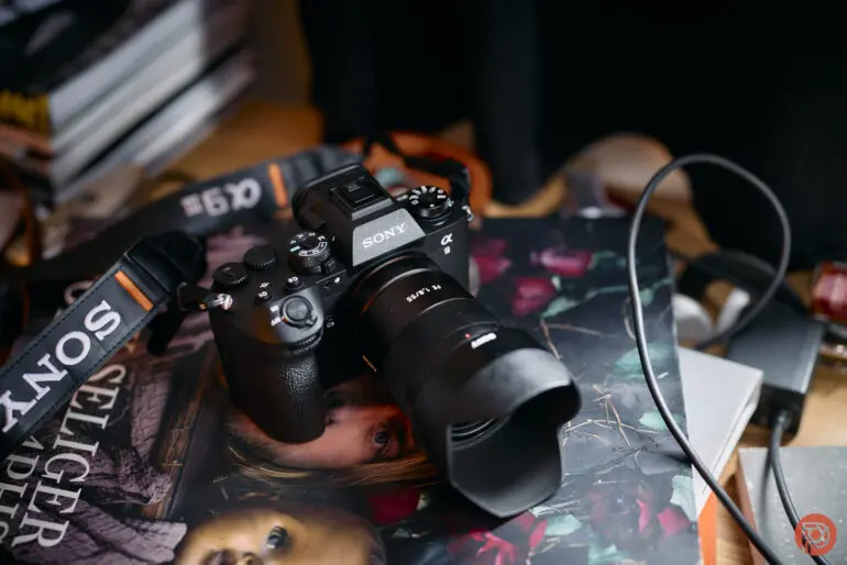دوربین سونی آلفا با لنز بر روی یک کتاب و سایر وسایل روی سطح شلوغ قرار گرفته است.