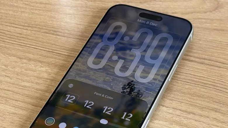 آیفون روی میز چوبی که صفحه قفل iOS با ساعت دیجیتال را نشان می‌دهد